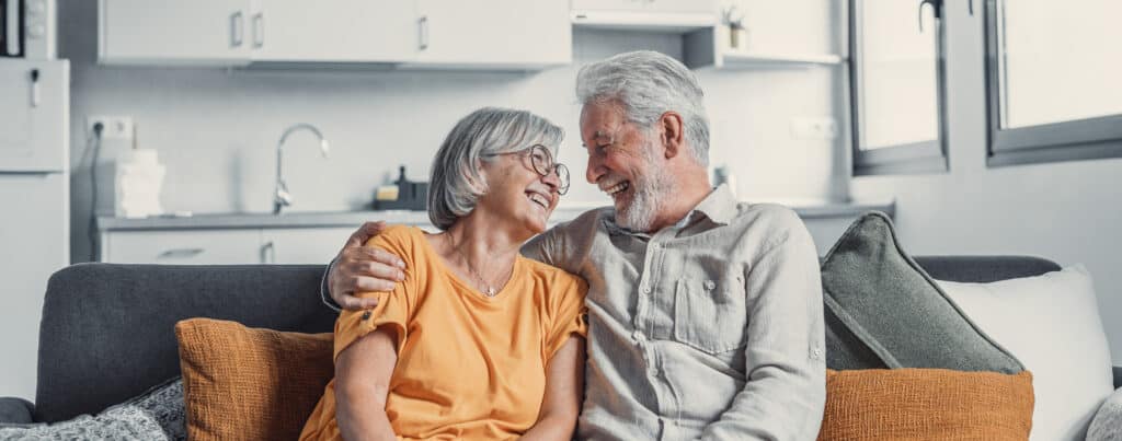 Happy mature husband and wife sit rest on couch at home hugging and cuddling, show care affection, smiling senior loving couple relax on sofa have fun, enjoy tender romantic family weekend together.