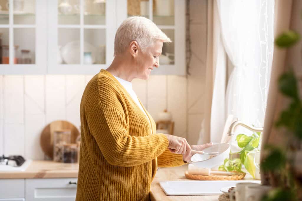 Happy senior woman washing dishes in kitchen